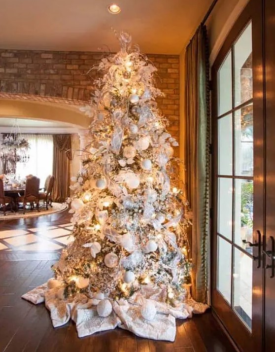 a winter wonderland Christmas tree with white and silver ornaments, lights, ribbons, branches and white blankets covering the base of the tree