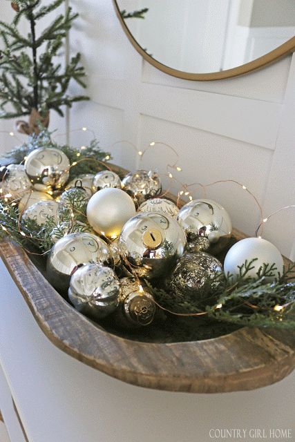 a wooden bowl with silver ornaments, evergreens and lights is a lovely holiday decoration that can be used in various places