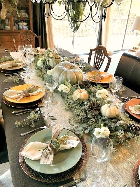 a woodland or rustic Thanksgiving centerpiece of greenery, pinecones, green and white pumpkins plus blooms