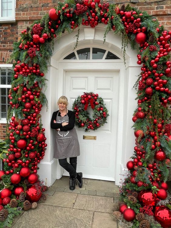 an amazing home entrance with evergreen garlands and red ornaments, pinecones and a matching wreath on the door for Christmas