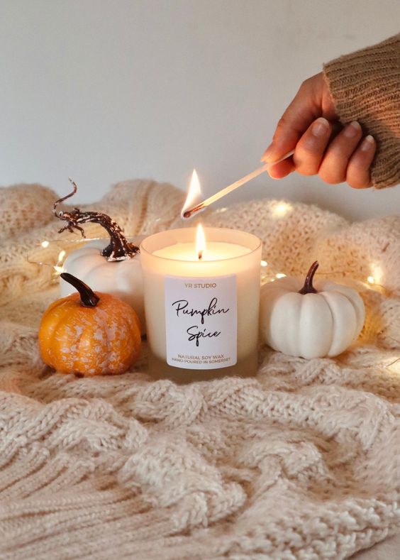 an easy fall or Thanksgiving decoration of a neutral knit blanket, some faux pumpkins, lights and a candle in a jar