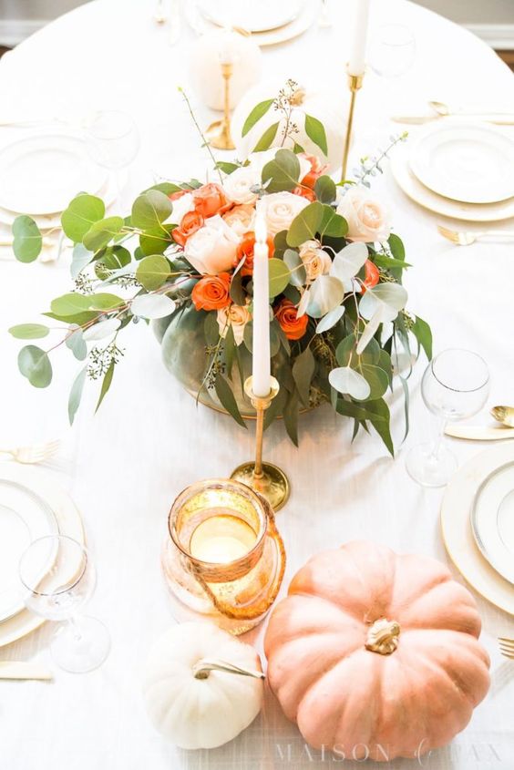 an elegant Thanksgiving centerpiece of a green pumpkin, orange and blush blooms and greenery plus tall and thin candles