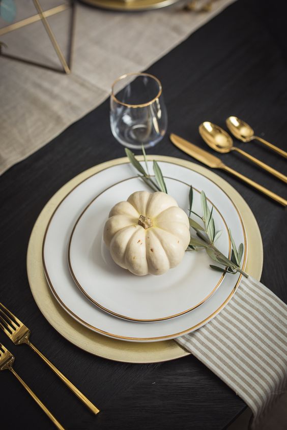 an elegant and chic Thanksgiving place setting with a gold charger, gold rimmed plates, gold cutlery and a striped napkin plus a pumpkin