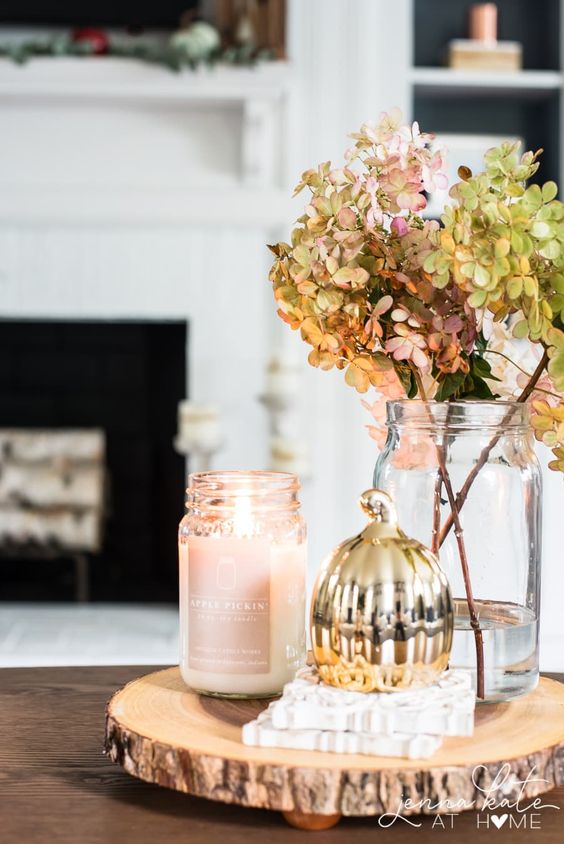 an elegant fall or Thanksgiving decoration of a wood slice, a candle in a jar, a gilded pumpkin and some dried hydrangeas in a jar