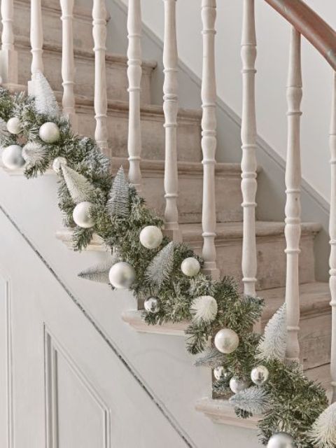 an evergreen garland with silver and matte silver ornaments and bottle brush Christmas trees is a chic idea for styling a staircase