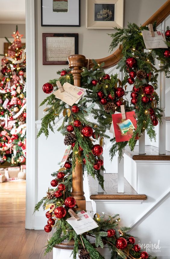 beautiful Christmas banister decor with an evergreen garland, red ornaments, pinecones and Christmas postcards