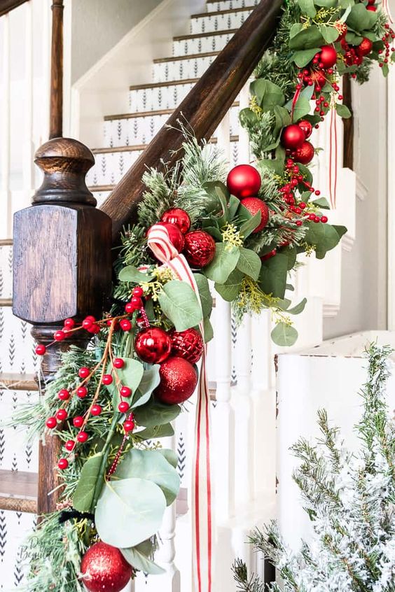 chic Christmas banister decor with evergreens and foliage, red ornaments, berries and a red and white striped ribbon is cool