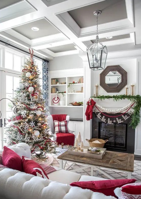 cozy and chic Christmas living room decor with red pillows, bead and pompom garlands, a fir garland, a flocked Christmas tree with lights, snowflakes and letters
