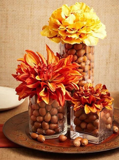 glass vases filled with acorns and with bright blooms on top are a lovely rustic centerpiece idea for Thanksgiving