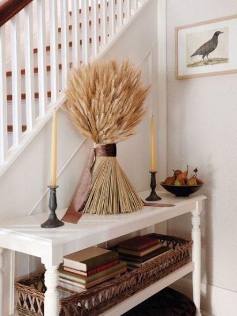 lovely Thanksgiving decor with a bunch of wheat and tall and thin candles in dark metal candleholders plus faux pears in a bowl for a vintage feel
