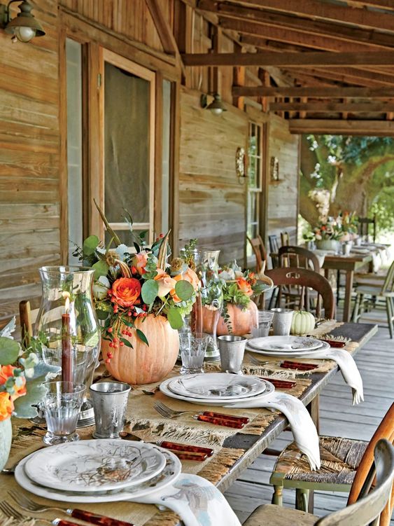 lovely bright Thanksgiving centerpieces of orange pumpkins, orange blooms and greenery, berries and feathers