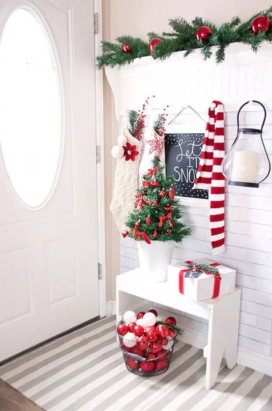 red and white ornaments in a wire bucket, red ornaments for a tiny tree and white stockings create beautiful Christmas entryway decor