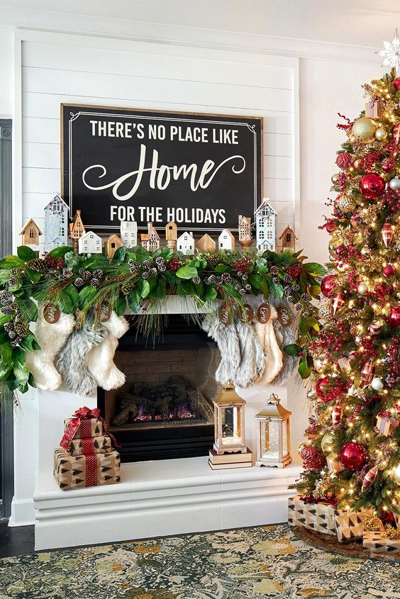 a Christmas mantel with an evergreen and snowy pinecone garland, mini houses and stockings plus a Christmas tree with matching decor