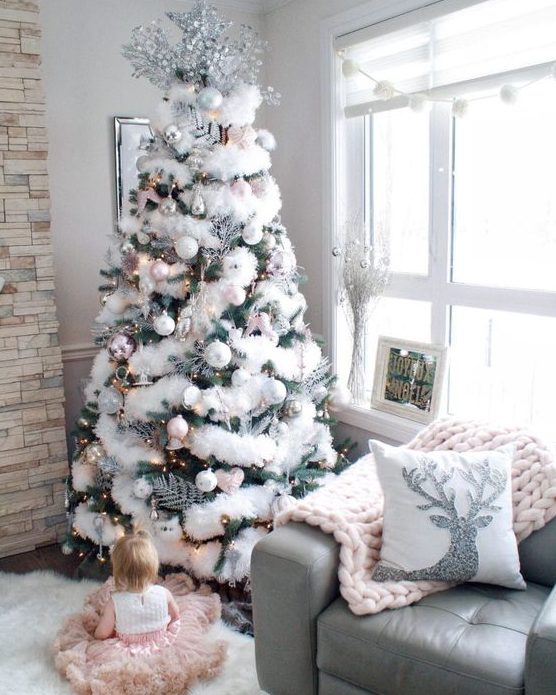 a Christmas tree decorated with white and silver ornaments, lights and fluffy fur garlands plus a large silver topper
