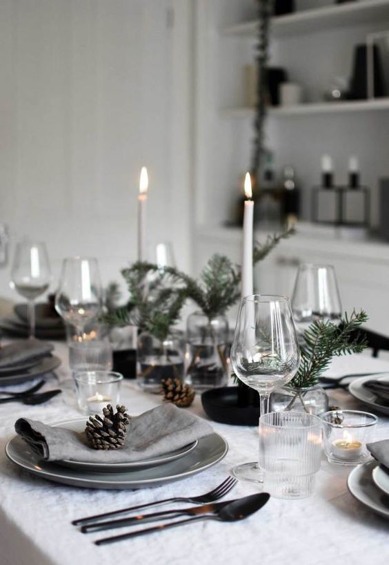 a Nordic Christmas table with tall and thin candles, evergreens, grey plates, neutral linens and simple glasses