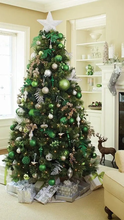 a beautiful forest glam Christmas tree with lots of green and white ornaments of various sizes, silver leaves, lights and branches plus a white star on top