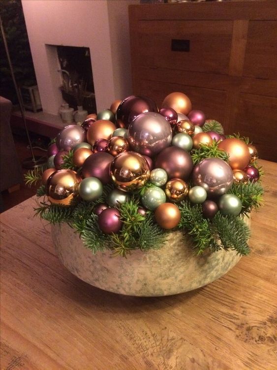 a bowl with a whole arrangement of metallic and pink ornaments and evergreens is a cool holiday centerpiece