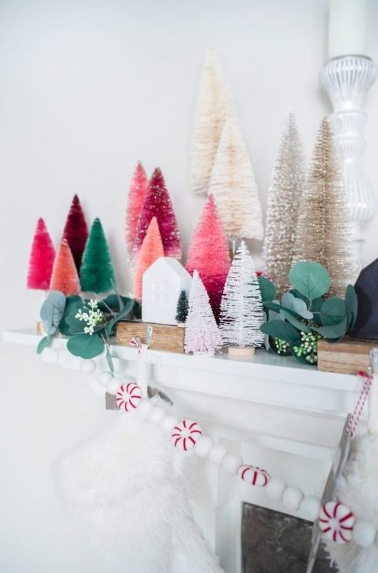 a chic Christmas mantel decorated with colorful bottle brush trees, fau greenery, a peppermint garland and mini houses