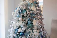 a classic flocked Christmas tree with light blue, navy, white snowball-inspired ornaments, lights, pompoms and stars is wow