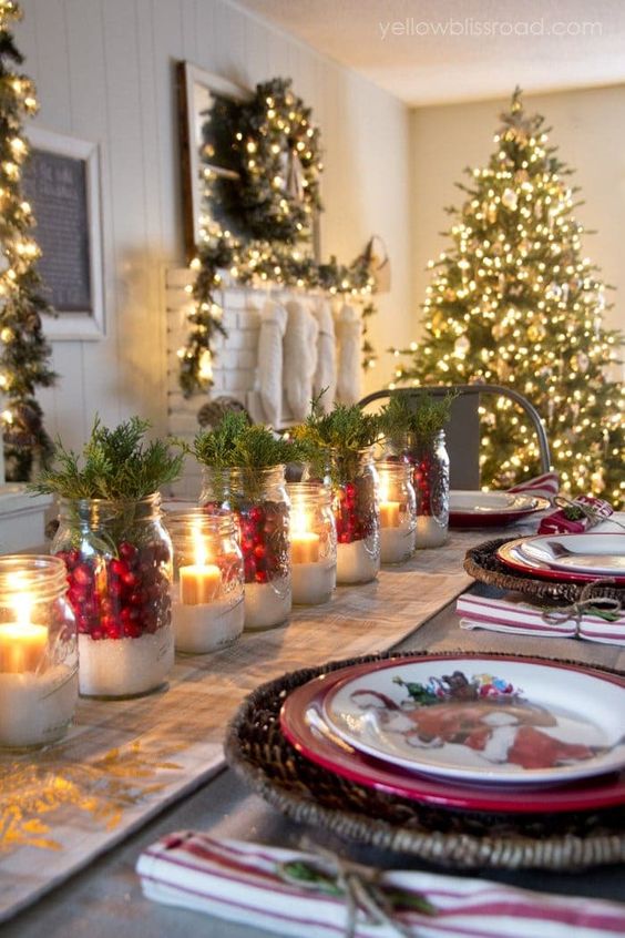 a cozy Christmas table with woven placemats, jars with faux snow, berries, greenery and candles and printed plates is bright and cool