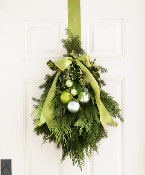 a creative Christmas decoration of evergreens, green and silver ornaments, leaves and ribbons is a cool idea to style your front door