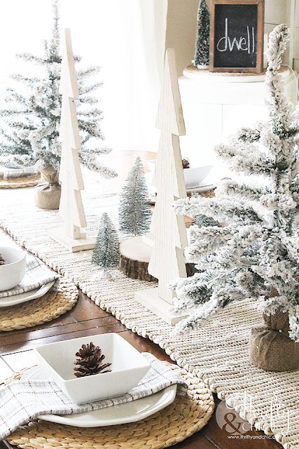 a farmhouse Christmas tablescape with a woven table runner and placemats, flocked and plywood Christmas trees, white porcelain and pinecones
