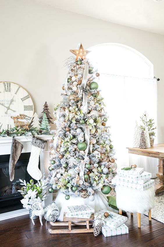 a flocked Christmas tree decorated with green, brown and gold ornaments, ribbons, a marquee light star on top and some leaves