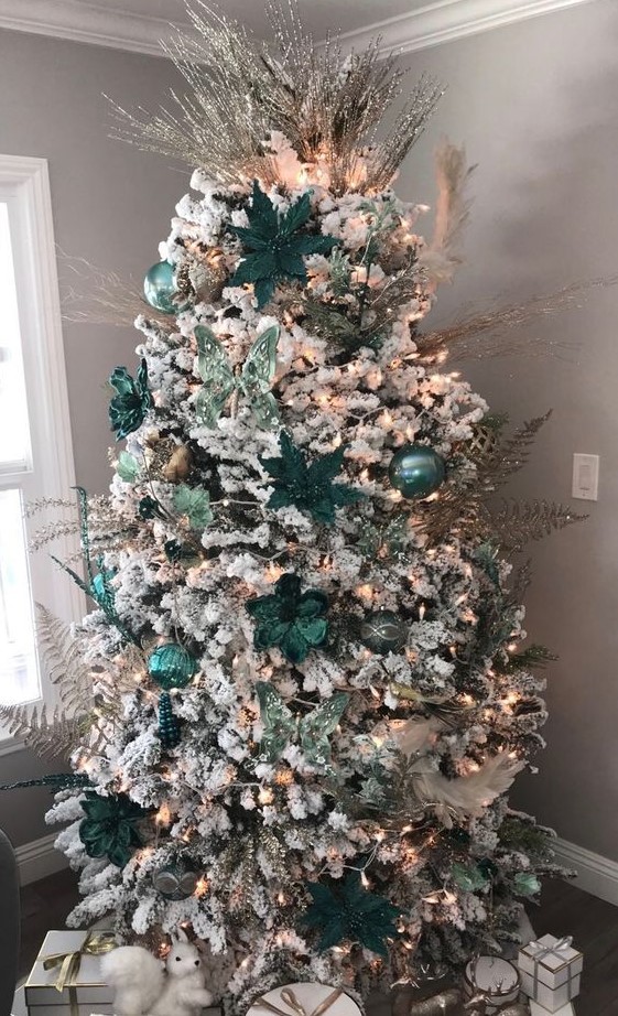 a flocked Christmas tree decorated with light and dark green ornaments, butterflies, fabric blooms and silver leaves and twigs