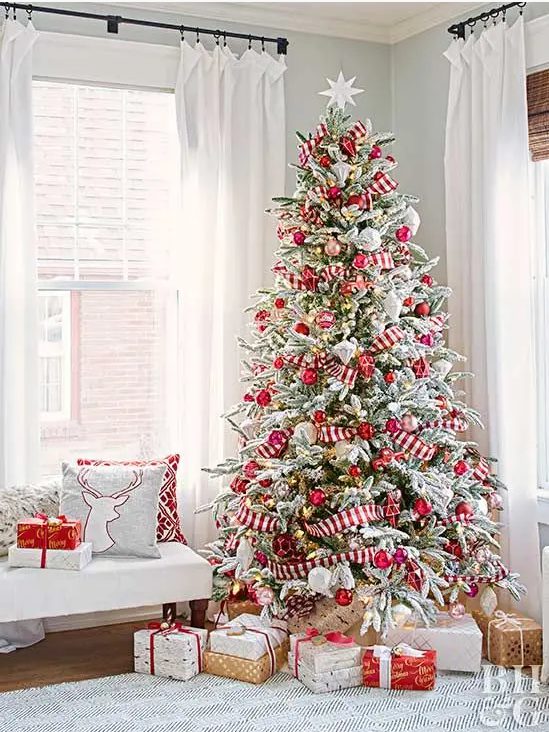 a flocked Christmas tree with lights, red and metallic ornaments and red and white striped ribbons plus a star