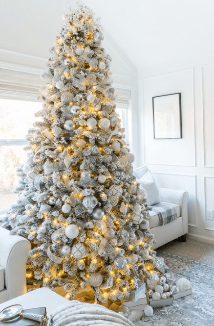 a flocked Christmas tree with metallic and white ornaments, lights and white and silver ribbons is a luxurious piece