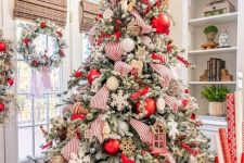 a flocked Christmas tree with white, red and twine ornaments, snowflakes, striped ribbons and berry branches is wow