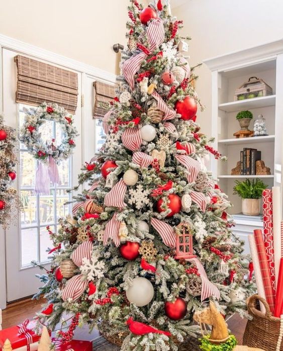 a flocked Christmas tree with white, red and twine ornaments, snowflakes, striped ribbons and berry branches is wow