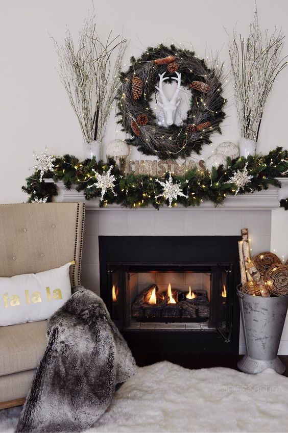 a glam Christmas mantel with an evergreen, snowflake and light garland, a matching wreath, snowballs and branches in vases