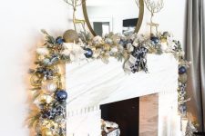 a glam Christmas mantel witha gold, silver and navy Christmas ornament garland and tall gold deer figurines is a chic idea to rock