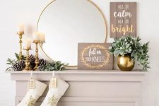 a glam and rustic Christmas mantel with large pinecones, gilded candle holders and a vase, a sign and a mirror