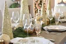 a glam gold and white Christmas tablescape with gold glitter Christmas trees, gold placemats, white napkins, evergreens and ornaments
