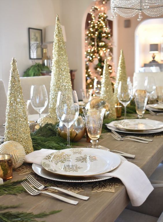 a glam gold and white Christmas tablescape with gold glitter Christmas trees, gold placemats, white napkins, evergreens and ornaments