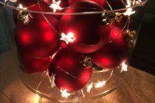 a glass bowl with red Christmas ornaments and a star light garland is a cool winter decoration