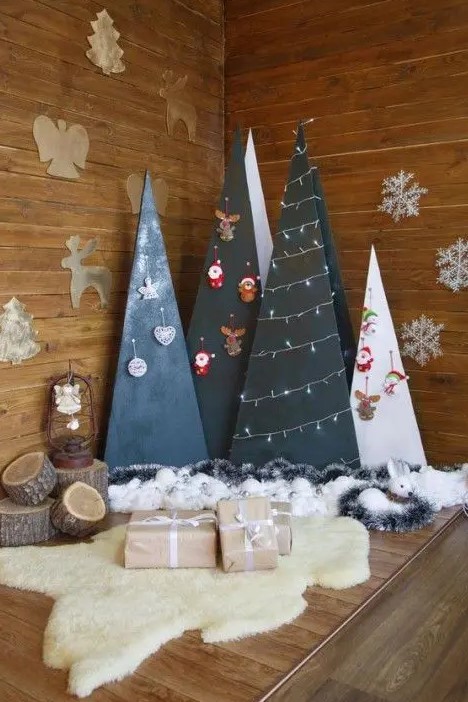 a group of plywood Christmas trees in black and white decorated with lights and ornaments hanging on hooks