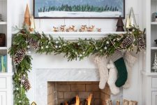 a lovely Christmas mantel with an evergreen and pinecone garland with stars, stockings, mini trees and lots of deer figurines