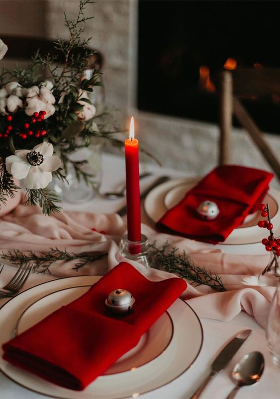 a lovely holiday tablescape with a blush runner, white blooms and red berries, red napkins and candles, simple gold-rimmed plates
