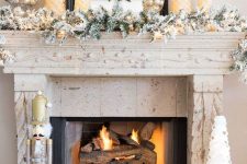 a lovely snowy Christmas mantel with a snowy evergreen garland with lights, mini Christmas trees and silver ornaments in jars