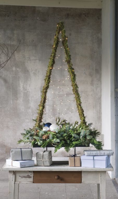 a metal frame tabletop Christmas tree covered with green and with evergreens, pinecones and ornaments in the planter, with lights