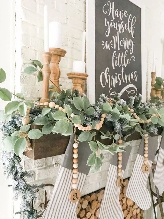 a pretty farmhouse Christmas mantel with a greenery garland and wooden beads, candles in wooden candleholders and striped stockings
