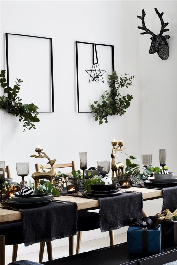 a pretty glam Christmas tablescape with black plates and bowls, smoked glasses, black napkins, gold deer and lots of fresh greenery