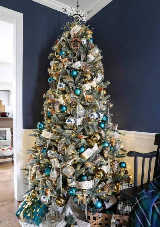 a pretty woodland glam Christmas tree with green, teal, gold ornaments, shiny metallic pinecones, a white printed ribbon and some deer ornaments
