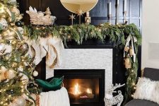 a refined dressed up Christmas mantel with a lush evergreen garland with lights, oversized bells and ribbons and candles in chic candleholders