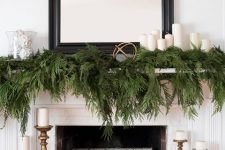 a refined modern rustic Christmas mantel with lots of fern, pillar candles, white Christmas ornaments and candles in wooden candleholders