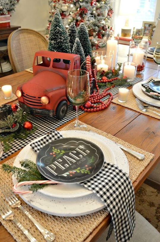 a retro Christmas table with buffalo check linens, black and white plates, a red truck with bottle brush Christmas trees and red ornaments