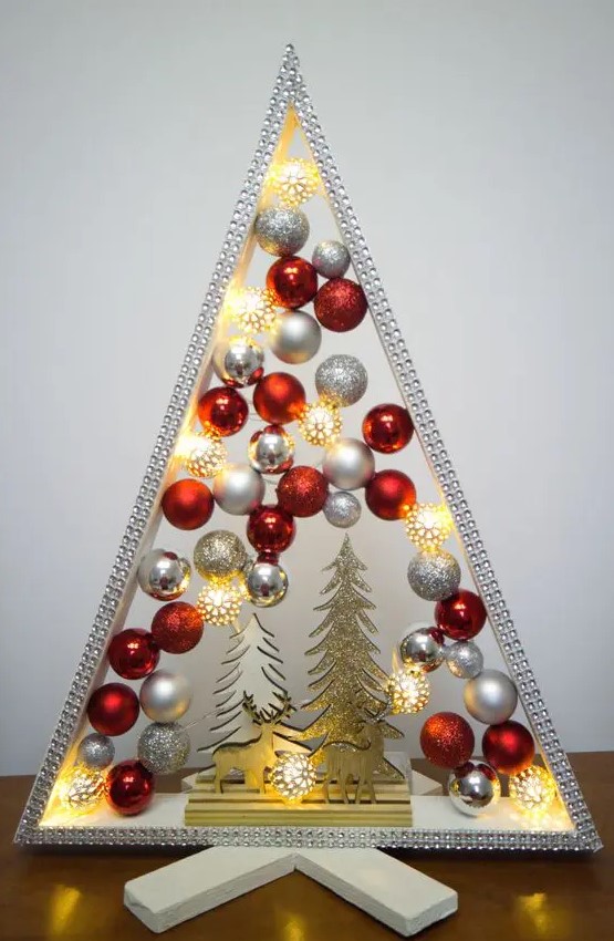 a shiny and glam tabletop Christmas tree with silver, glitter and red ornaments, some glitter trees and deer and lights inside